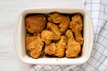Tasty homemade oven baked fried chicken in a dish over white wooden background, overhead view. Flat lay, top view, from above.