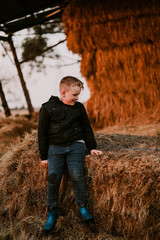 Naklejka na ściany i meble Young boy sitting on hay stack on country property