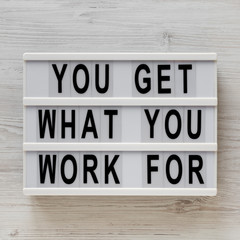 'You get what you work for' words on a modern board on a white wooden background, top view. Overhead, from above, flat lay. Close-up.