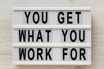 'You get what you work for' words on a lightbox on a white wooden background, top view. Overhead, from above, flat lay. Close-up.