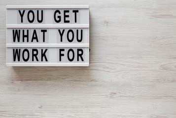 'You get what you work for' words on a lightbox on a white wooden background, top view. Overhead, from above, flat lay. Space for text.