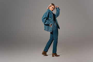 attractive woman in denim jacket and jeans looking at camera on grey background