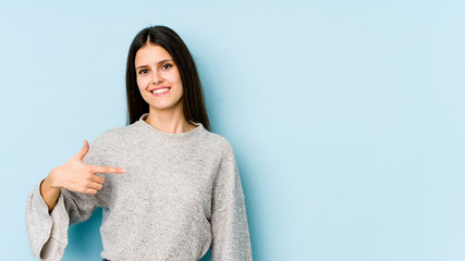 Fototapeta premium Young caucasian woman isolated on blue background person pointing by hand to a shirt copy space, proud and confident