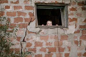 Young boy looking through window of old red brick shed