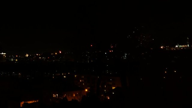 Timelapse of fireworks exploding in the night sky at different locations around a city with red and gold flashes in the distance