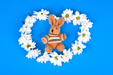 hare in flowers on a blue background. blue in the background. View from above. Spring Easter. Flowers and a knitted rabbit.