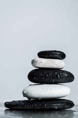 Close up view of stacked black and white zen stones on wet glass isolated on grey