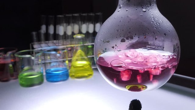 close up alcohol lamp is boiling red chemical liquid changing to purple or violet color in flask with lab glassware on black background. laboratory research and development