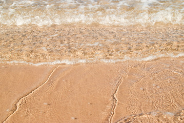 Fototapeta na wymiar Shallow water on the shore as gentle waves break over warm yellow sand at the beach