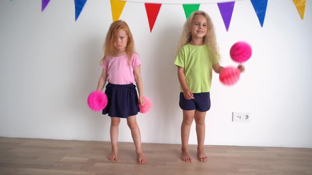 Creative little girls pretending cheerleaders holding pink pompon paper balls