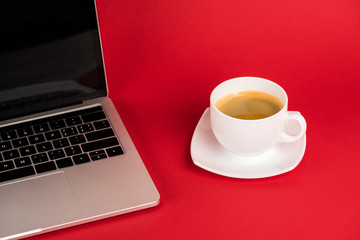 Laptop with blank screen and coffee cup on saucer on red background
