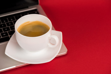 Close up view of cup of coffee on laptop on red surface