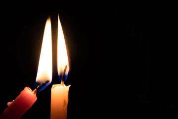 Meaningful image of Two Candles Lighting each other with black background for message and focus on orange candle. Concept of Celebration, Birthday, Homage, Tribute, Support and Help in difficult times