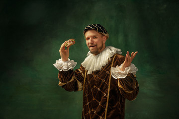 Shocking food. Portrait of medieval young man in vintage clothing with wooden frame on dark...