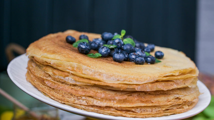 Pancakes with blueberries and honey on a plate, on wooden roofing. Traditional pastries for the Russian festival of Maslenitsa. free space for text. Close-up shot.