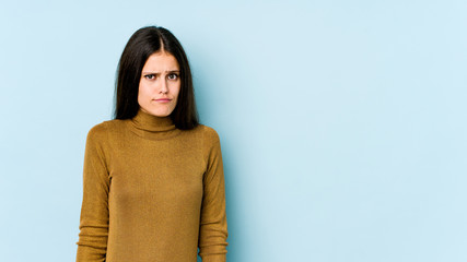 Young caucasian woman isolated on blue background shrugs shoulders and open eyes confused.