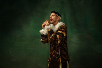 Secret taste. Portrait of medieval young man in vintage clothing with wooden frame on dark background. Male model as a duke, prince, royal person. Concept of comparison of eras, modern, fashion.