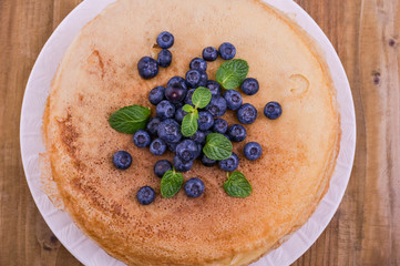 Pancakes with blueberries and honey on a plate, on wooden roofing. Traditional pastries for the Russian festival of Maslenitsa. free space for text. Close-up shot. Above