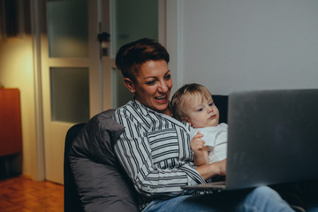 mother and her baby boy using laptop relaxed on sofa