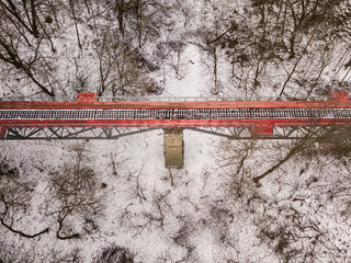 Aerial drone view. Bright red railway bridge among a snowy park.