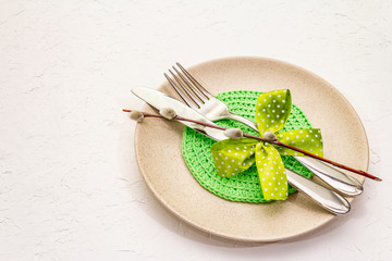 Easter table setting on textured white putty background. Spring holiday card template. Cutlery, knitted napkin, bow, willow seals