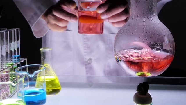 alcohol lamp is boiling red chemical liquid in flask with scientist stirring some sample in beaker and pouring to flask, make chemical reaction. laboratory research and development concept.