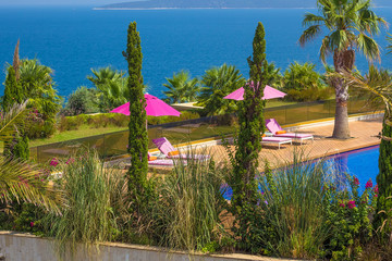 Pink umbrellas and deck chairs near water pool on the territory of luxury Turkish hotel in Bodrum, Mugla, Turkey. Turkish summer vacation, rich resort. Travel concept