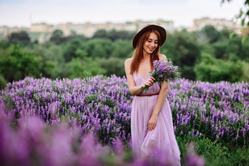 Red-haired girl in a hat lies in the grass with purple flowers. Young woman smile in nature. lady...