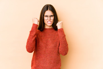 Young caucasian woman isolated on beige background showing fist to camera, aggressive facial expression.