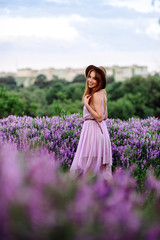 Red-haired girl in a hat lies in the grass with purple flowers. Young woman smile in nature. lady walks on a lavender field.