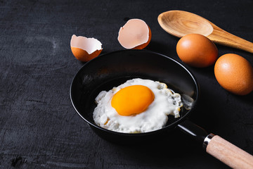 Fried eggs in a frying pan and egg shell  for breakfast on a black background.