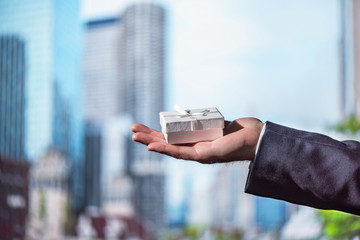 A man holding in his hands white gift box tied against the city skyscrapers.