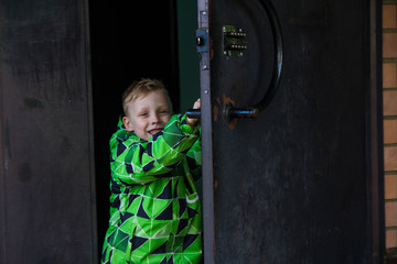 The blond boy opened the door, and walks into the entrance of the house. The child smiles.