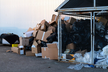 Paper boxes next to a garbage bin. Stack of paper waste outdoor in the city. Paper recycling, nobody
