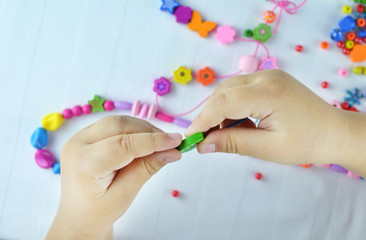 Close-up of the hand of the Little girl who makes an ornament from beads on white desktop. Art,...