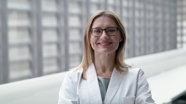 Portrait of female doctor standing on corridor, looking at camera.