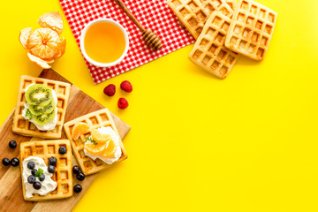 Breakfast with freashly baked belgian waffles on yellow background top-down frame copy space