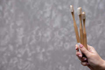 Three white bamboo toothbrushes in a hand on a gray concrete background. close-up. soft light. friendly eco.