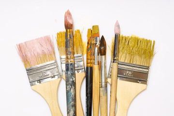 Various artistic brushes with paint on white background. Messy creative equipment.