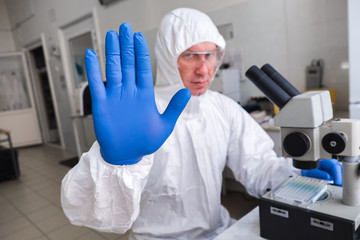 A biologist in a White protective suit and glasses works with a microscope in the laboratory. The...