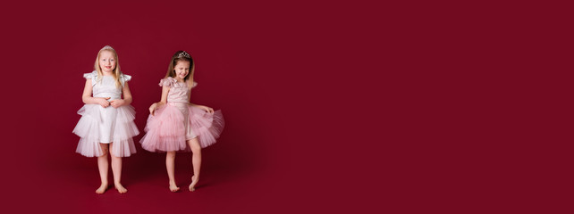 Beautiful little girls princess playing in luxury pink, white and silver dresses isolated on red background. Funny face, different emotions © Lena May