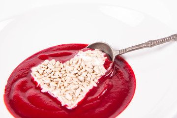 Beetroot cream soup decorated with a heart made of yoghurt and sunflower seeds eaten with a vintage spoon