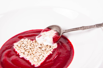 Beetroot cream soup decorated with a heart made of yoghurt and sunflower seeds eaten with a vintage spoon