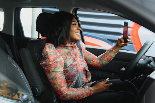 Beautiful black woman doing selfie in the car. Lips young woman taking selfie picture with smart phone camera outdoors in car