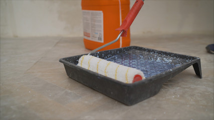 A worker pours a primer from an orange canister.. Worker pouring a primer in a paint tray