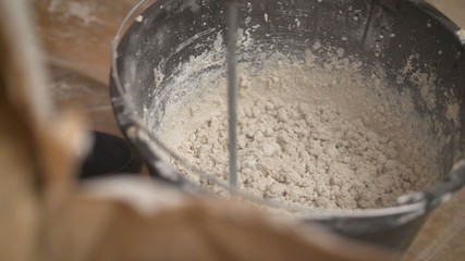 Construction worker man stirs the mixture in the bucket construction for alignment and putty walls of the apartment with the help of a powerful drill. Bucket with dry mortar for plastering 
