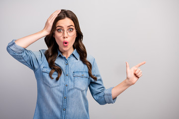 Photo of crazy business lady open mouth indicate finger empty space advising low prices arm on head wear specs casual jeans denim shirt isolated grey color background