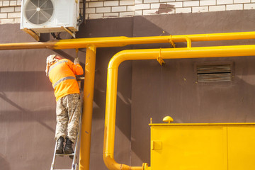 A man paints a gas pipe with yellow paint.