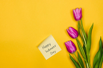 womens day background. pink tulips and sticky note on yellow background