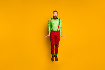 Fototapeta na wymiar Full length photo of attractive funky guy open mouth jumping high rejoicing shocked wear green shirt red suspenders pants socks footwear isolated yellow color background